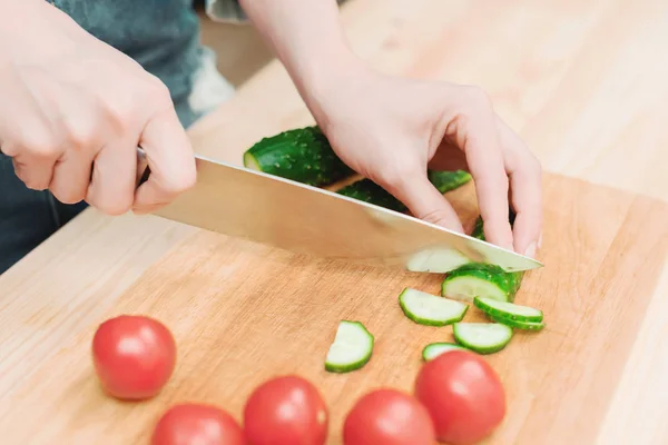 Close-up of female hands cut into fresh cut cucumbers on a wooden cutting board next to pink tomatoes. The concept of homemade vegetarian cuisine and healthy eating and lifestyle — Stock Photo, Image