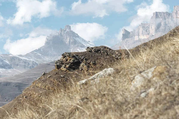 Jesienne górskiej pożółkłe stoki i trawa w górach z części pokryte śniegiem stoki w słoneczny dzień przeciw błękitne niebo i białe chmury i epickie skały. Koncepcja idealna — Zdjęcie stockowe
