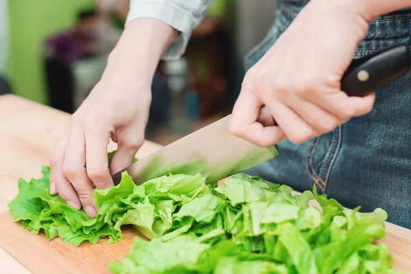 Primer plano Las manos femeninas cortan una ensalada de plantas verdes cocinando ensalada de verduras en una tabla de cortar de madera en casa. El concepto de vegetarianismo y estilos de vida saludables — Foto de Stock