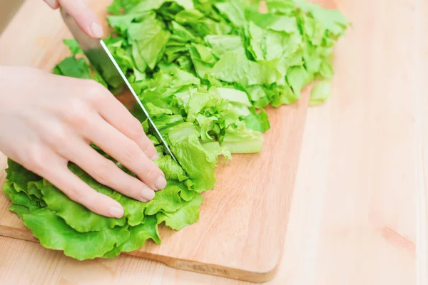 Primer plano Las manos femeninas cortan una ensalada de plantas verdes cocinando ensalada de verduras en una tabla de cortar de madera en casa. El concepto de vegetarianismo y estilos de vida saludables — Foto de Stock
