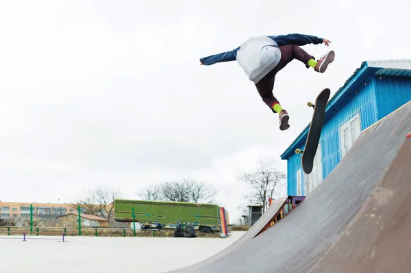 Um adolescente skatista de chapéu faz um truque com um salto na rampa. Um skatista está voando no ar — Fotografia de Stock