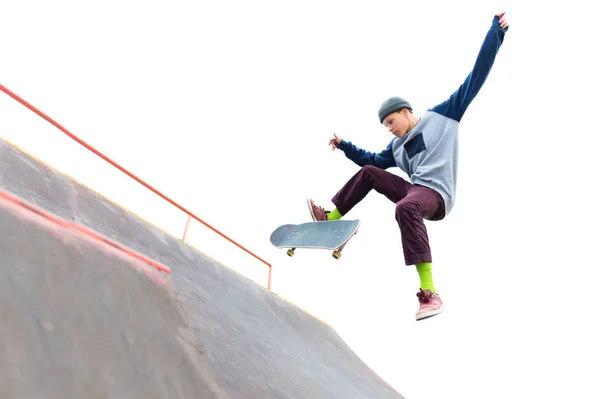 Lo skateboarder adolescente nel berretto fa un trucco con un salto sulla rampa nello skatepark. Pattinatore isolato e rampa su sfondo bianco — Foto Stock