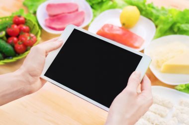 Bir ev mutfak masasına sağlıklı yemek çevrili bir boş ekran ile bir tablet bilgisayar tutan eller en iyi görmek. İşlenecek parçanın mobil uygulamanın tasarımına eklemek için