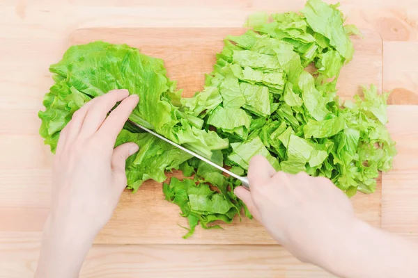 Primer plano Las manos femeninas cortan una ensalada de plantas verdes cocinando ensalada de verduras en una tabla de cortar de madera en casa. El concepto de vegetarianismo y estilos de vida saludables — Foto de Stock