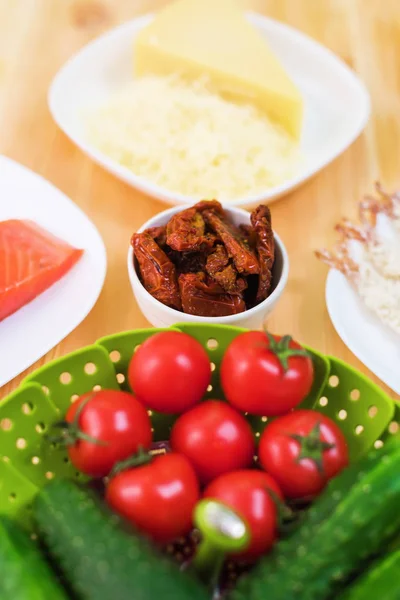 Ainda vida de comida crua em chapas brancas em uma mesa de madeira. O salmão congelado em uma chapa ao lado de pepinos e tomates ralou o queijo e os camarões crus no pão. Antecedentes do tema da alimentação saudável — Fotografia de Stock