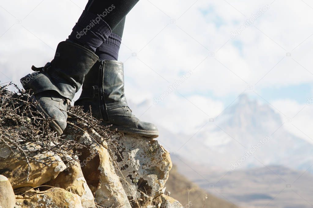 Close-up of female feet in vintage boots stand on a rock in the mountains against the background of an epic landscape of fairy-tale rocks and clouds on the holoomed sky. The concept of relaxation in