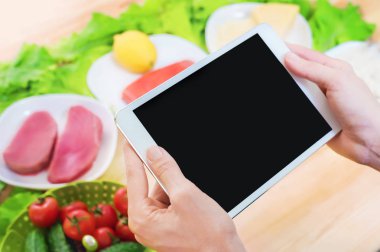 Bir ev mutfak masasına sağlıklı yemek çevrili bir boş ekran ile bir tablet bilgisayar tutan eller en iyi görmek. İşlenecek parçanın mobil uygulamanın tasarımına eklemek için
