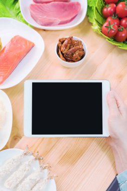 Bir ev mutfak masasına sağlıklı yemek çevrili bir boş ekran ile bir tablet bilgisayar tutan eller en iyi görmek. İşlenecek parçanın mobil uygulamanın tasarımına eklemek için