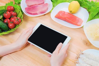 Bir ev mutfak masasına sağlıklı yemek çevrili bir boş ekran ile bir tablet bilgisayar tutan eller en iyi görmek. İşlenecek parçanın mobil uygulamanın tasarımına eklemek için
