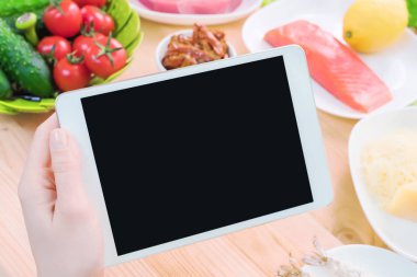 Bir ev mutfak masasına sağlıklı yemek çevrili bir boş ekran ile bir tablet bilgisayar tutan eller en iyi görmek. İşlenecek parçanın mobil uygulamanın tasarımına eklemek için