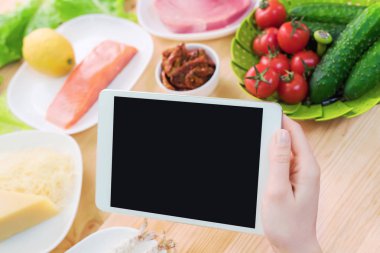 Bir ev mutfak masasına sağlıklı yemek çevrili bir boş ekran ile bir tablet bilgisayar tutan eller en iyi görmek. İşlenecek parçanın mobil uygulamanın tasarımına eklemek için