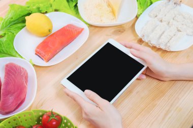 Bir ev mutfak masasına sağlıklı yemek çevrili bir boş ekran ile bir tablet bilgisayar tutan eller en iyi görmek. İşlenecek parçanın mobil uygulamanın tasarımına eklemek için