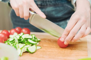 Yakın çekim narin eller çeyrek bir ahşap tahtada evde domates büyük bir bıçakla kesti. Ev mutfak. Sağlıklı beslenme. Vejetaryenlik kavramı