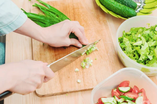 Крупным планом нежные женские руки режут на деревянной доске стебли зеленого лука, делающего салат. Концепция вегетарианской здоровой пищи и образа жизни. Приготовление здоровой пищи дома — стоковое фото