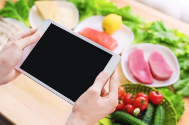 Bir ev mutfak masasına sağlıklı yemek çevrili bir boş ekran ile bir tablet bilgisayar tutan eller en iyi görmek. İşlenecek parçanın mobil uygulamanın tasarımına eklemek için