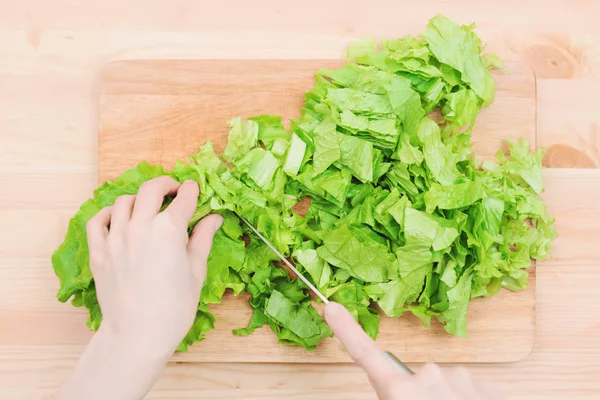 Primer plano Las manos femeninas cortan una ensalada de plantas verdes cocinando ensalada de verduras en una tabla de cortar de madera en casa. El concepto de vegetarianismo y estilos de vida saludables — Foto de Stock