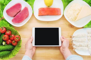 Bir ev mutfak masasına sağlıklı yemek çevrili bir boş ekran ile bir tablet bilgisayar tutan eller en iyi görmek. İşlenecek parçanın mobil uygulamanın tasarımına eklemek için