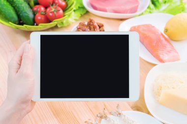 Bir ev mutfak masasına sağlıklı yemek çevrili bir boş ekran ile bir tablet bilgisayar tutan eller en iyi görmek. İşlenecek parçanın mobil uygulamanın tasarımına eklemek için