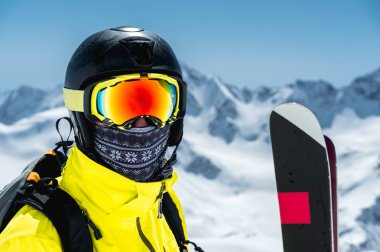 Bir kayakçı koruyucu bir kask ve gözlük - maske ve bir eşarp kayaklar Kafkasya karla kaplı dağlar karşı yanındaki büyük bir portresi. Kayak