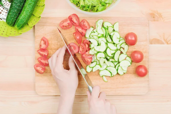 Primer plano Delicadas manos femeninas cortan un cuchillo grande con tomates en un cuarto en una tabla de madera en casa. Cocina casera. Alimentación saludable. El concepto de vegetarianismo — Foto de Stock