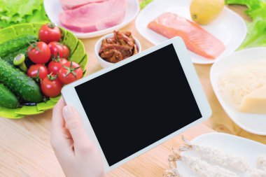 Bir ev mutfak masasına sağlıklı yemek çevrili bir boş ekran ile bir tablet bilgisayar tutan eller en iyi görmek. İşlenecek parçanın mobil uygulamanın tasarımına eklemek için