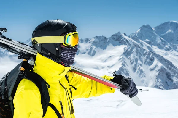 Um grande retrato de um esquiador em um capacete protetor e óculos é uma máscara e um lenço com esquis em seu ombro nas montanhas cobertas de neve do Cáucaso. Esqui , — Fotografia de Stock