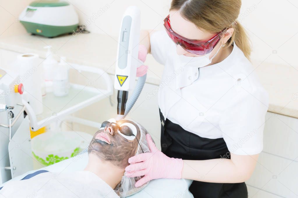 The cosmetician girl in goggles makes the procedure of carbon peeling with the help of a cosmetology laser. Carbon face peeling procedure. Laser pulses clean skin of the face. Hardware cosmetology