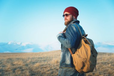 Düşünceli bir şık hipster güneş gözlüğü sakallı ve gün batımında Kafkasya'da karla kaplı Elbruz Dağı arka plan üzerinde bir sırt çantası ile bir şapka portre