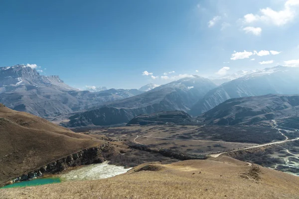 Paisaje de alta montaña del Cáucaso Norte. Una instantánea de la altura de un lago y un camino de tierra sobre un fondo. Cielo azul con nubes — Foto de Stock