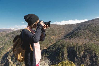 Yakın çekim portre sarışın kızla dağlarda fotoğraf çekimi bir dijital Slr fotoğraf makinesi. Şık freelance fotoğrafçı dağ beyaz gezi sırt çantası ile