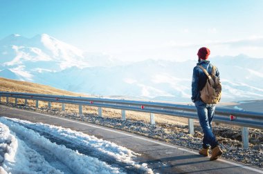 Güneş gözlüğü vintage bir sırt çantası ile şık bir sakallı hippi güneşli bir günde asfalt yolda yürür. Otostop ve hiking kavramı