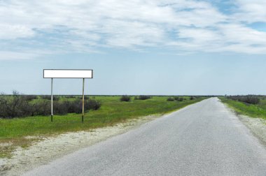Boş eski yol işareti için bir şehir veya köy adını alan kırsal mavi bir gökyüzü ve beyaz bulutlar tarafından yeşil çim çevrili karşı road yakınındaki doldurulur