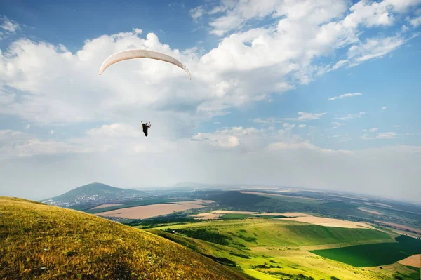 Un parapente vuela en el cielo en un traje de capullo en un parapente sobre el campo caucásico con colinas y montañas. Parapente Concepto Deportivo — Foto de Stock