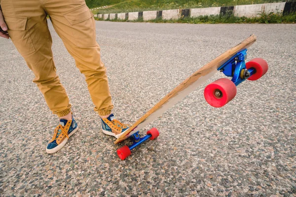 Közeli fel a férfi lábak rongyot cipők egy Longboard a háttérben aszfalt naplementekor. Nagy gördeszka az ember lába. Ifjúsági szabadidőkoncepció — Stock Fotó