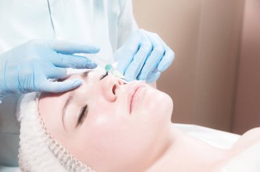 Yakın plan çekici genç kadın yaşlanma karşıtı yüz enjeksiyonları yaptırıyor. Bir klinikte ya da kuaförde sakince yatıyor. Deneyimli genç bir kozmetikçi kadın kırışıklıklarını şırınganın hyaluronik asidiyle dolduruyor.