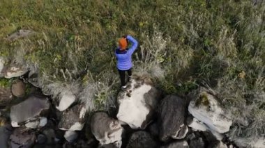 Bir kız nehir kenarındaki bir taşın üzerinde duran ve büyük destansı bir şelaleyi fotoğraflayan profesyonel bir manzara fotoğrafçısı. Hava görüntüsü. Kuzey Kafkasya