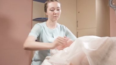 Girl beautician in a mask and gloves makes a salubrious facial massage to an attractive woman. New generation cosmetology massage