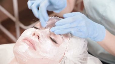 Kozmetik uzmanı olan kız deriyi temizleme ve nemlendirme işlemini gerçekleştiriyor. Bir kadın yüzü için özel bir fırçayla maske takın. Cildine önem veriyorsun..