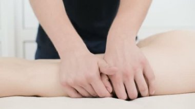 Yakın çekim bir erkek fizyoterapist pamuk bir delikanlı yanında profesyonel bir spa salonunda genç bir kadının kalça ve kalça ısınmak için hafif bir masaj yapıyor. 4k masaj vücut bakım konsepti