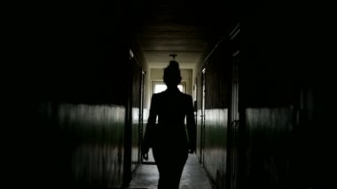 Arkadan görülebilen bir kadın silueti. Fosforlu. Bir kadın figürü karanlık bir koridorda yürüyor, kameradan uzaklaşıyor..