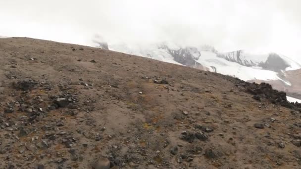Повітряний вид на низький політ над вулканічними породами в горах на тлі гори Ельбрус і великого льодовика. Гірська подорож і рельєфна концепція Uhd 4k — стокове відео