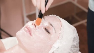 Kozmetik uzmanı olan kız deriyi temizleme ve nemlendirme işlemini gerçekleştiriyor. Bir kadın yüzü için özel bir fırçayla maske takın. Cildine önem veriyorsun..