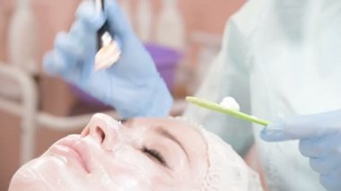 Kozmetik uzmanı olan kız deriyi temizleme ve nemlendirme işlemini gerçekleştiriyor. Bir kadın yüzü için özel bir fırçayla maske takın. Cildine önem veriyorsun..