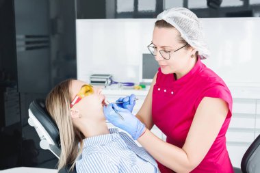 Dişçi ofisinde. Gözlüklü bir kadın diş hekimi genç bir kız hastanın çenebir döküm yapmaya hazırlanıyor. Bakım temiz ağız
