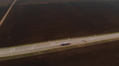 Kırsal asfalt otoyolun havadan görünüşü. Otoyol boyunca arabalar hareket ediyor. Arabalar ve kamyonlar bir kır yolu boyunca sürer. Karayolu hava görüntüleri. Yol kenarındaki tarlalar.