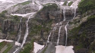 Hava aracı görüntüsü birkaç şelalenin yüksek dağlardaki dik kayalıklardan aşağı aktığını ve yemyeşil ve erimemiş karlarla çevrili olduğunu gösteriyor. Kuzey Kafkasya 'nın doğa rezervleri kavramı