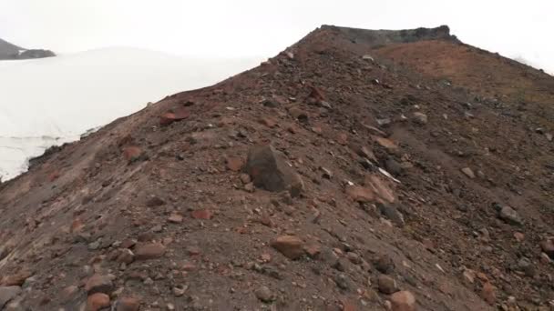 Luftaufnahme Tiefflug über Vulkangestein in den Bergen vor dem Hintergrund des Elbrus und eines großen Gletschers. Bergreise- und Kletterkonzept uhd 4k — Stockvideo