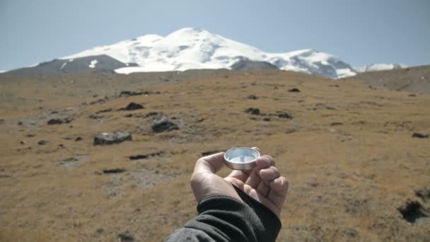 La vista en primera persona de una mano masculina sosteniendo una brújula magnética gira hacia un lado y busca la dirección correcta en el fondo de una montaña. El concepto de orientación — Vídeo de stock