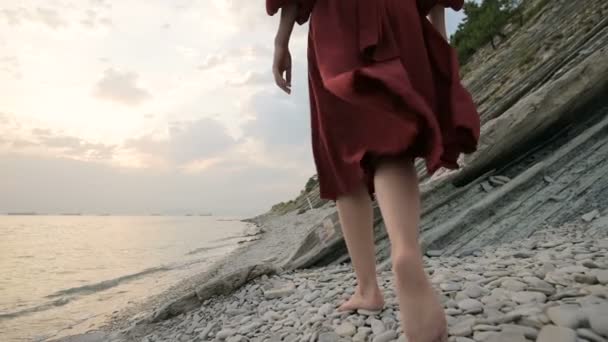 Descalza de chica yendo a la orilla arenosa con olas. Chica africana vestida de blanco caminando descalza sobre las olas del mar en la orilla al amanecer, de cerca. Seguimiento de disparo en cámara lenta — Vídeos de Stock