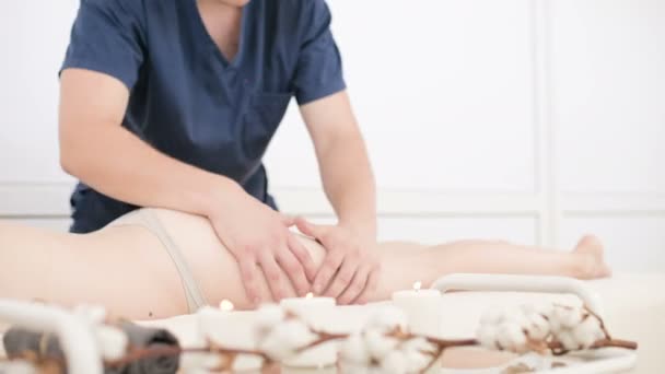 Close-up of a male physiotherapist doing a light massage to warm up the hips and buttocks of a young woman in a professional spa salon next to a sprig of cotton. 4K massage body care concept — Stock Video